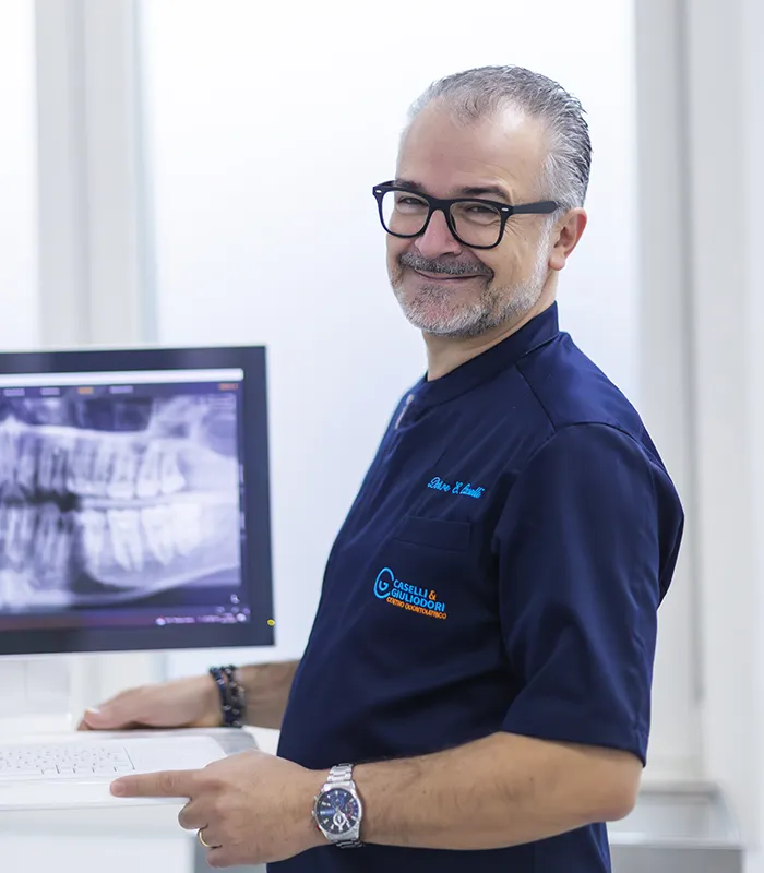 il dottor Caselli Erneto sorridente nel suo centro odontoiatrico, alle spalle un computer con radiografia dentale